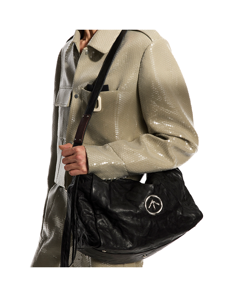 Black pleated leather crossbody bag with flap, logo emblem, and shoulder strap.