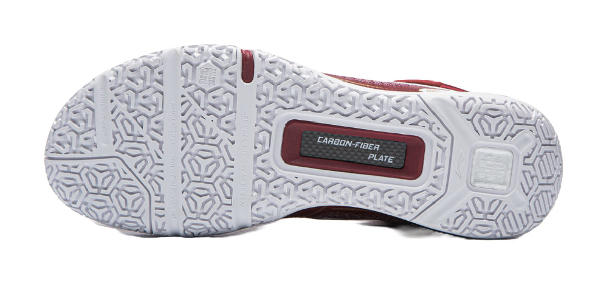 White outsole of red badminton shoe with hex tread pattern and CARBON-FIBER plate.