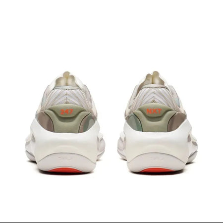 A pair of chunky low-top sneakers shown from the back, featuring a cream and light olive green upper with a thick white sole and a small orange accent near the heel.