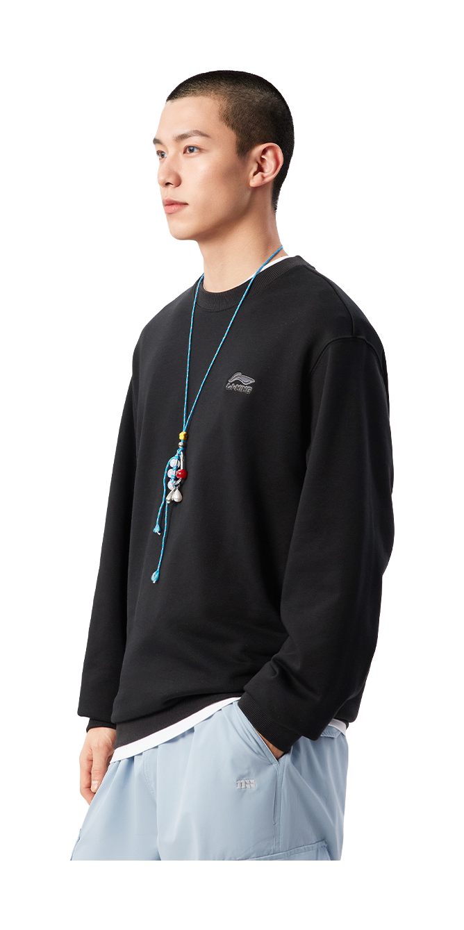 Black crewneck sweatshirt worn by model, side view; ribbed cuffs and hem, chest logo.