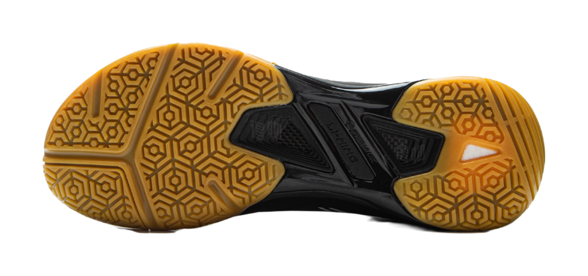 Black outsole of badminton shoe with gold hex traction pattern and molded center pods.