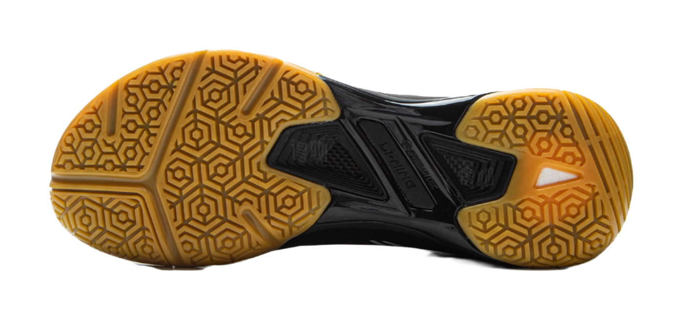Black outsole of badminton shoe with gold hex traction pattern and molded center pods.