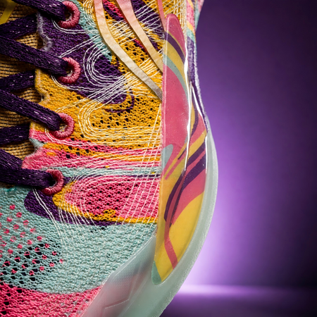 Close-up of basketball shoe side, multicolor embroidered mesh with purple laces and mint edge.