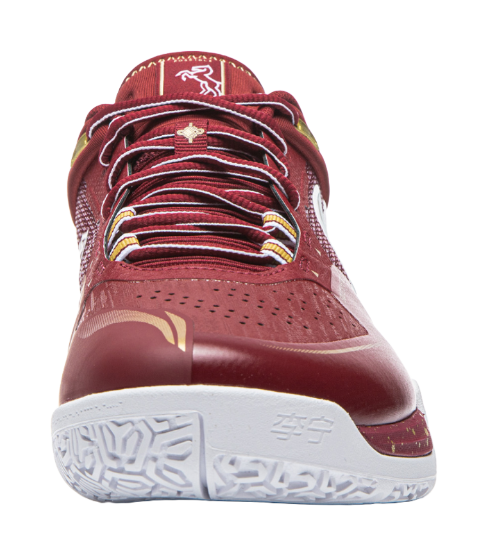 Red badminton shoe toe view with perforated forefoot, striped laces, and white outsole.