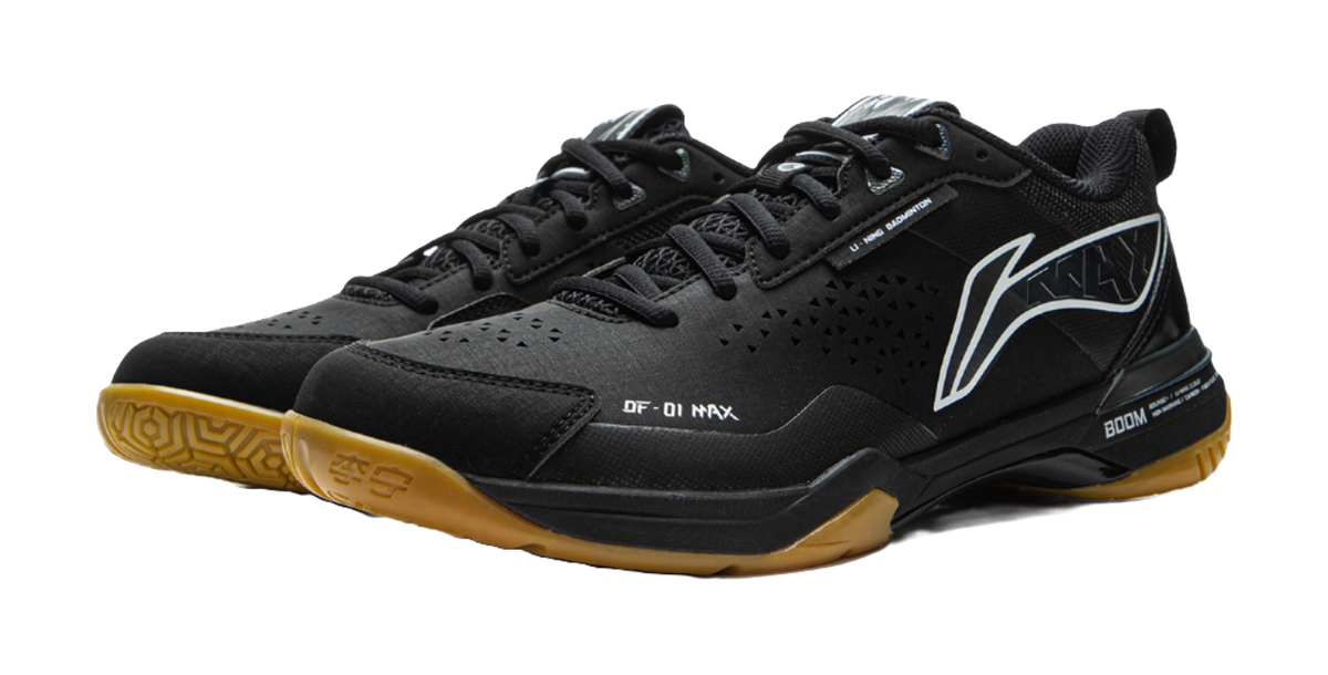 Black badminton shoe with gold outsole edge, black-and-white stripe, and BOOM sole panel.