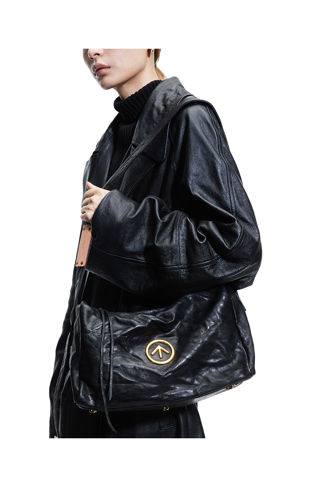 Black pleated leather crossbody bag with front flap and circular logo emblem.