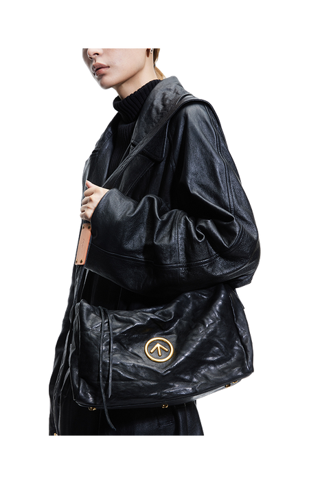 Black pleated leather crossbody bag with front flap and circular logo emblem.