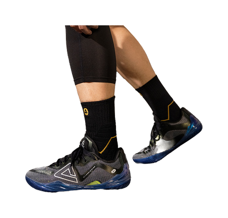 Basketball shoe on foot with black socks and blue-accent sole, black lace-up upper