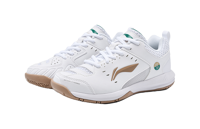 Pair of white lace-up badminton shoes with tan logo, green collar, brown outsole.