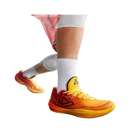 Basketball shoe on foot with orange/yellow lace-up upper and yellow collar patch
