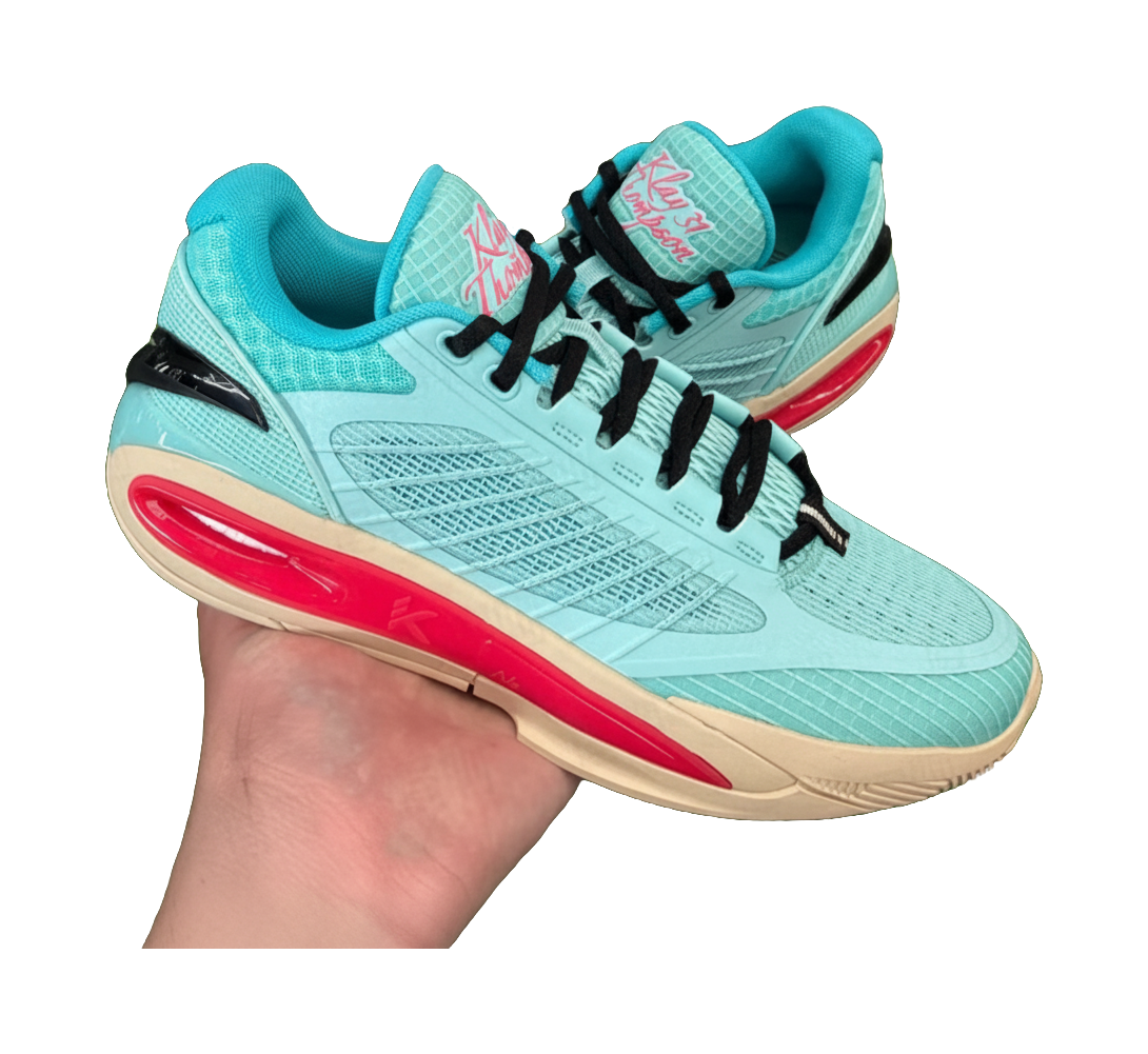 Turquoise low-top basketball shoe held in hand with black laces and red sole