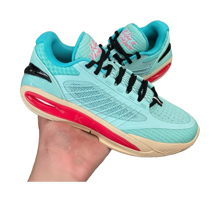 Turquoise low-top basketball shoe held in hand with black laces and red sole