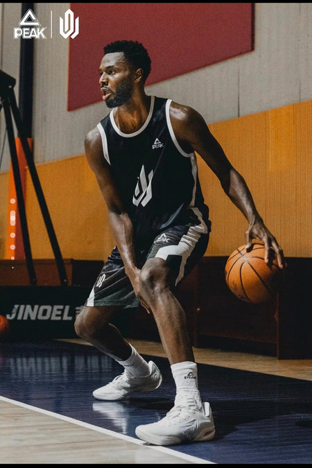 A basketball player in a black and white Spurs uniform dribbling an orange basketball on an indoor court, with visible Peak and Adidas logos on the jersey.