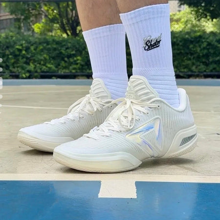 White athletic sneakers with white crew socks featuring a black Nike logo, shown on a person's feet on an outdoor basketball court.