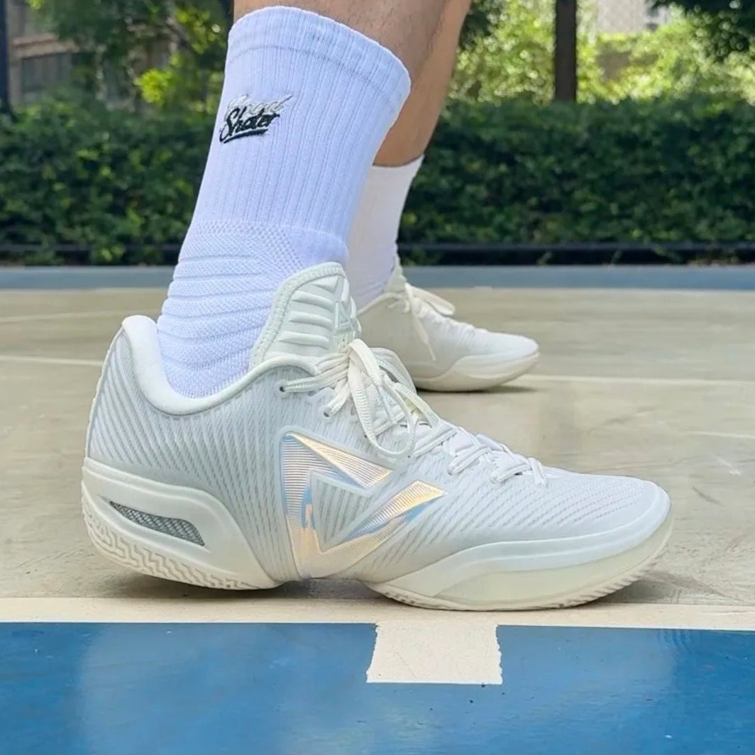 White athletic sneakers with white crew socks, shown on a basketball court with a person's legs visible.