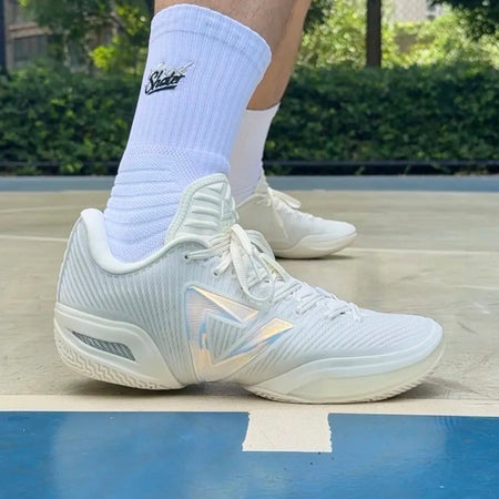 White athletic sneakers with white crew socks, shown on a basketball court with a person's legs visible.