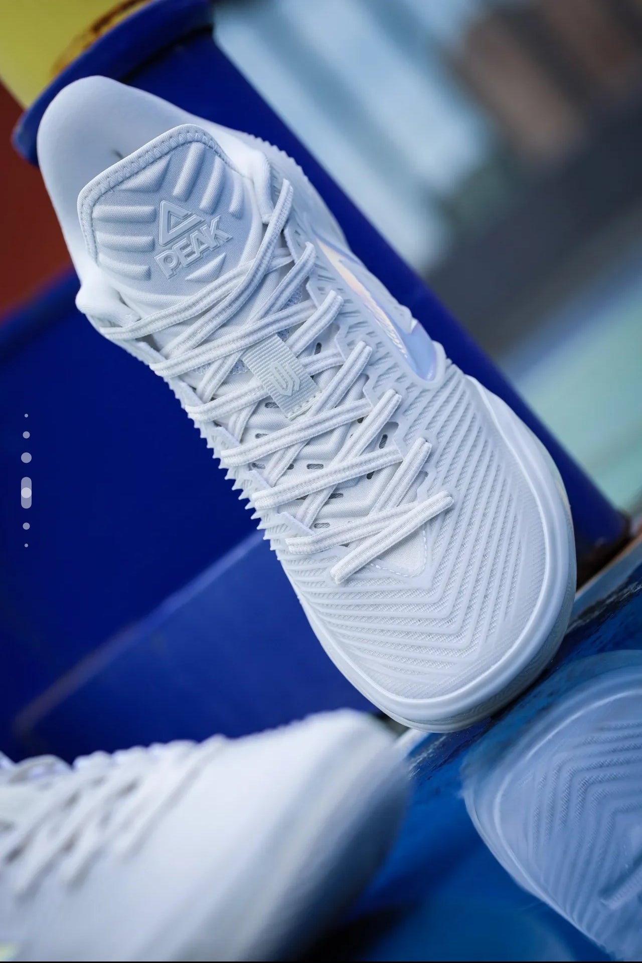 A close-up of a white Adidas basketball shoe with textured laces and a patterned upper, resting on a blue surface.
