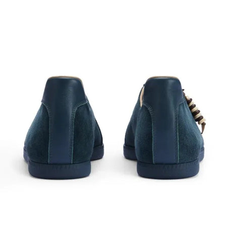A pair of dark navy blue suede low-top sneakers shown from the back, featuring a chunky block heel and a gold chain detail along the side, displayed on a white background.