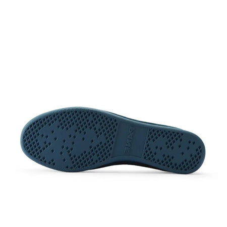 A close-up of a shoe sole, showing a dark teal-blue rubber outsole with a pattern of circular perforations, presented on a white background.