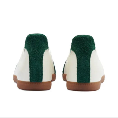 A pair of slip-on shoes shown from the back, featuring a white leather upper, a dark green plush collar, and a brown sole, set against a plain white background.
