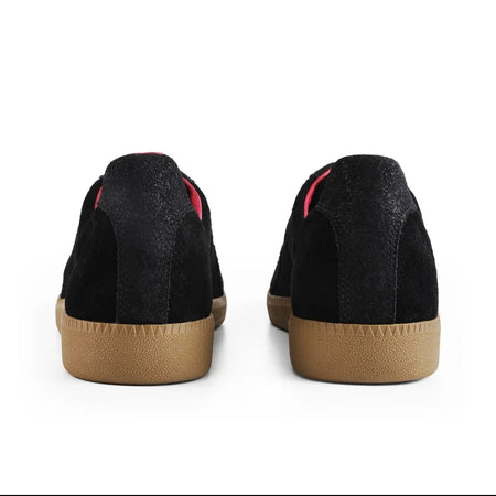 Black racerback low-top sneakers shown from the back, featuring a black textured suede upper, a thin red stripe detail near the collar, and a tan rubber sole.