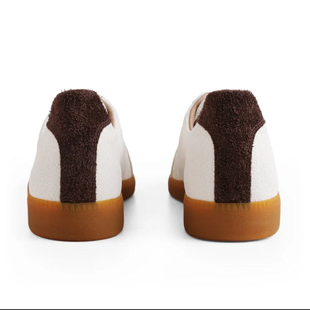 Rear view of a pair of white low-top sneakers with dark brown textured heel panels and gum soles, shown on a white background with black letterboxing and a phone interface overlay.