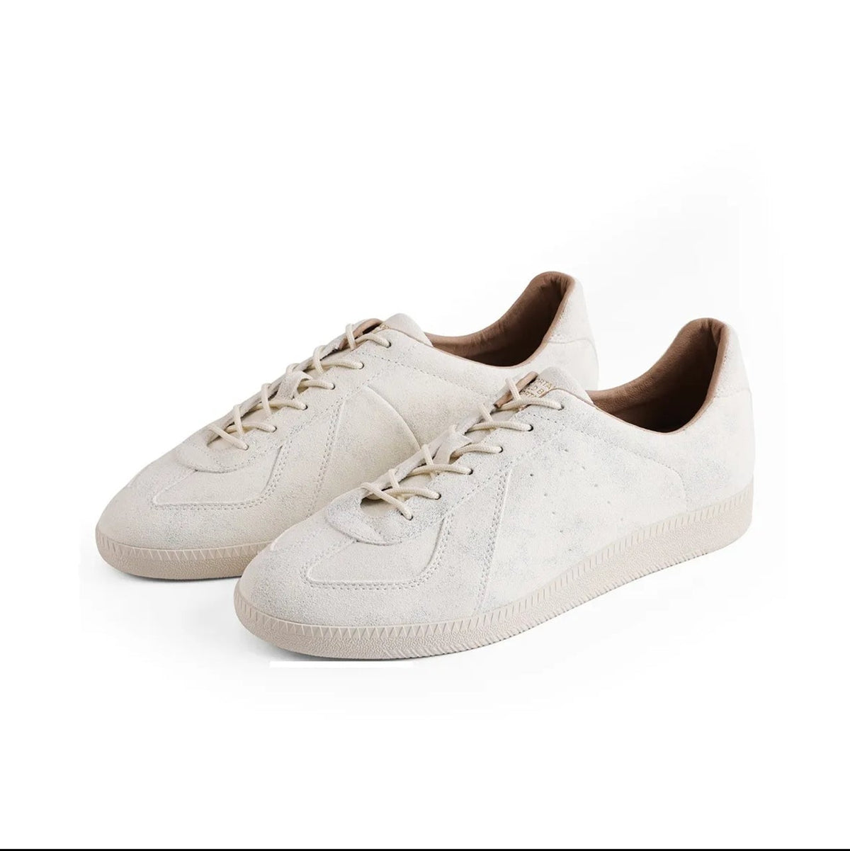 A pair of low-top lace-up sneakers in a light cream/off-white suede-like material, shown on a plain white background. The shoes have tonal laces and a dark brown interior lining.