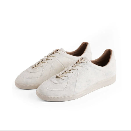 A pair of low-top lace-up sneakers in a light cream/off-white suede-like material, shown on a plain white background. The shoes have tonal laces and a dark brown interior lining.