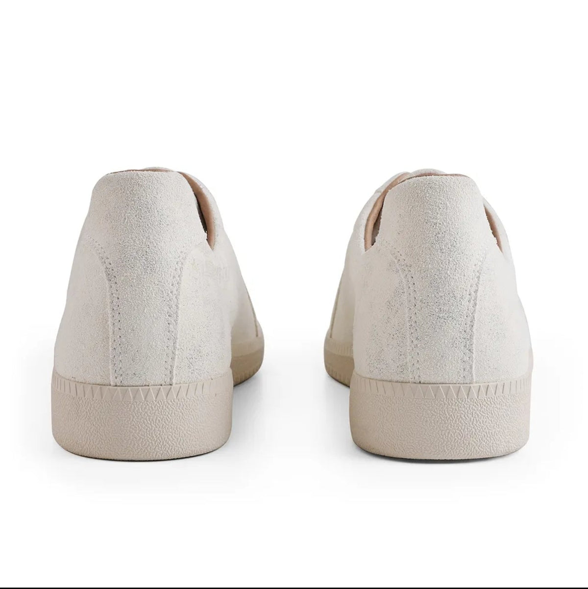 A pair of low-top slip-on sneakers shown from the back, in a warm off-white or cream color, displayed on a white background within a mobile app screenshot.