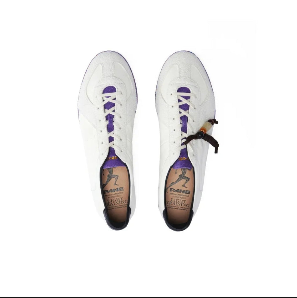A pair of white low-top sneakers shown from above on a white background, with purple laces and a small black-and-white patterned detail near the lace area. The insoles are tan and branded, but the brand text is not clearly legible.