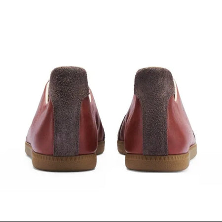 A pair of low-top slip-on shoes shown from the back, featuring reddish-brown leather uppers, dark brown fuzzy midsoles, and tan soles, displayed on a white background within a mobile app interface.