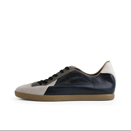 A low-top sneaker shown in side profile on a white background, with a black upper, light beige side panels, black laces, and a tan gum sole. The image appears to be a screenshot from a shopping app, with black bars and interface text around the product photo.