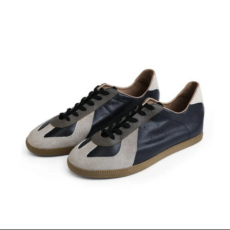 A pair of low-top sneakers shown on a white background within a mobile app screenshot. The shoes have navy blue leather uppers with light beige suede panels on the toe and side, black laces, and brown gum soles.