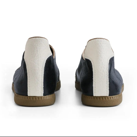 A pair of low-top casual shoes shown from the back, featuring navy blue leather panels, a vertical off-white stripe, and a tan rubber sole. The image is presented on a white background within a mobile app screenshot interface.