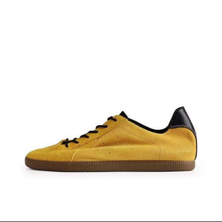 A yellow suede sneaker with black laces, a black heel tab, and a brown gum sole, shown against a white background. The image is a screenshot from a shopping app with black bars at the top and bottom and Chinese interface icons.