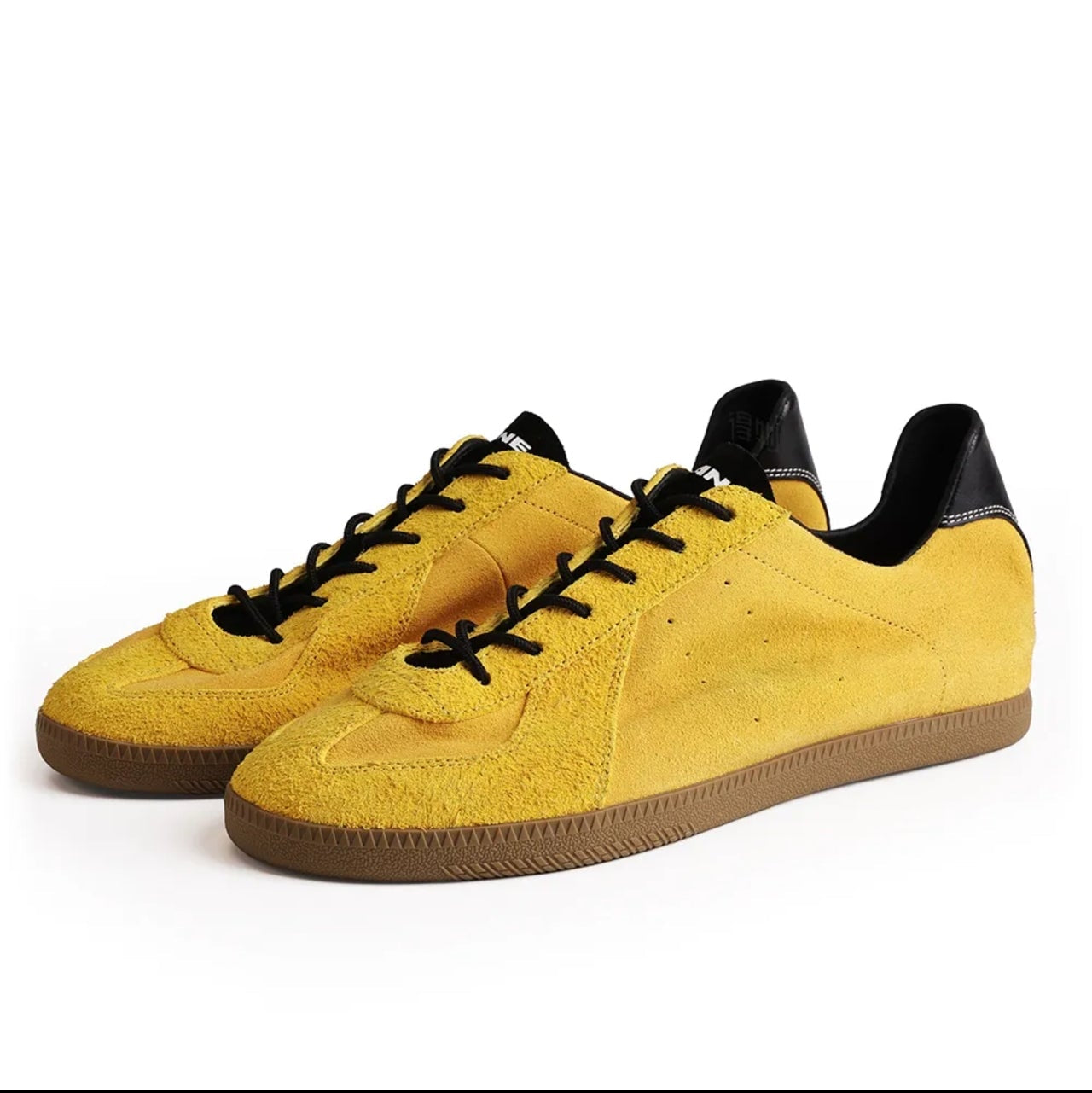 A pair of yellow suede low-top sneakers with black laces and black heel tabs, displayed on a white background. The image is a screenshot from a mobile shopping app, with black bars at the top and bottom and text reading 'HORNET 5215'.