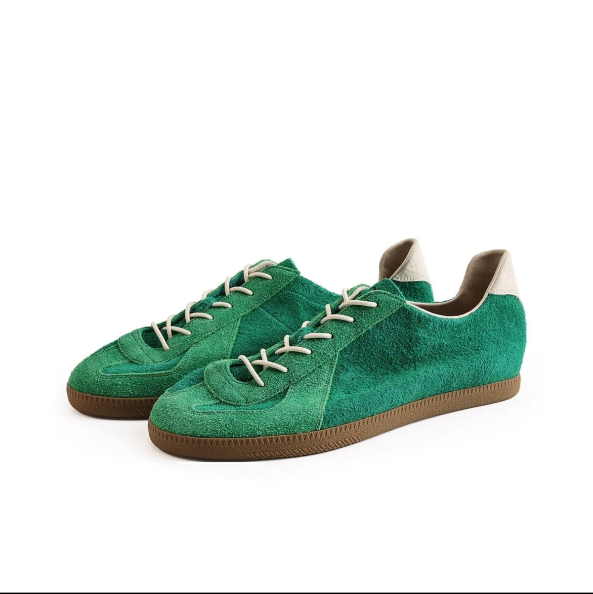 A pair of green suede low-top sneakers with beige laces and brown soles, shown on a white background within a mobile app screenshot.